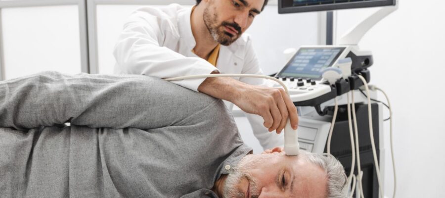 Clinician holds an ultrasound probe near a man's jaw while an imaging monitor displays scan data.