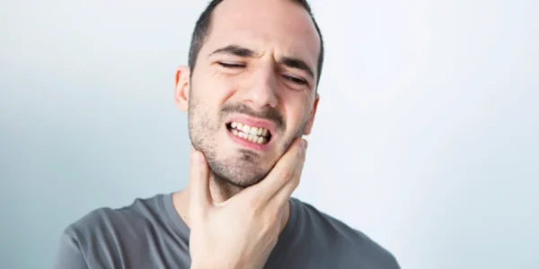 Man clenching his teeth while holding one side of his lower jaw with his hand.