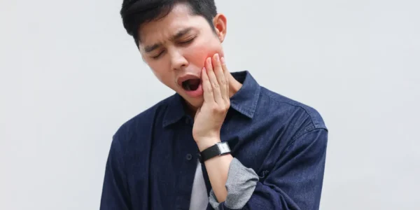 Man with eyes closed and mouth open while pressing one hand against the side of his jaw.