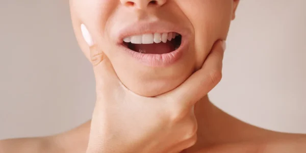 Close-up of a woman holding both sides of her jaw with her mouth open.
